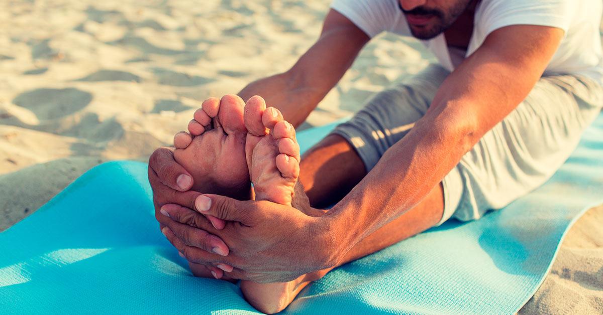 Man doing yoga on a mat in the sand